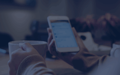 A woman's hands holding white coffee cup and mobile phone while using social media in modern loft cafe